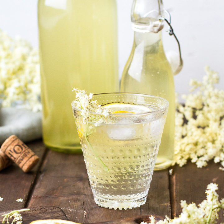 Homemade elderflower cordial in a clear glass with lemon wedge.