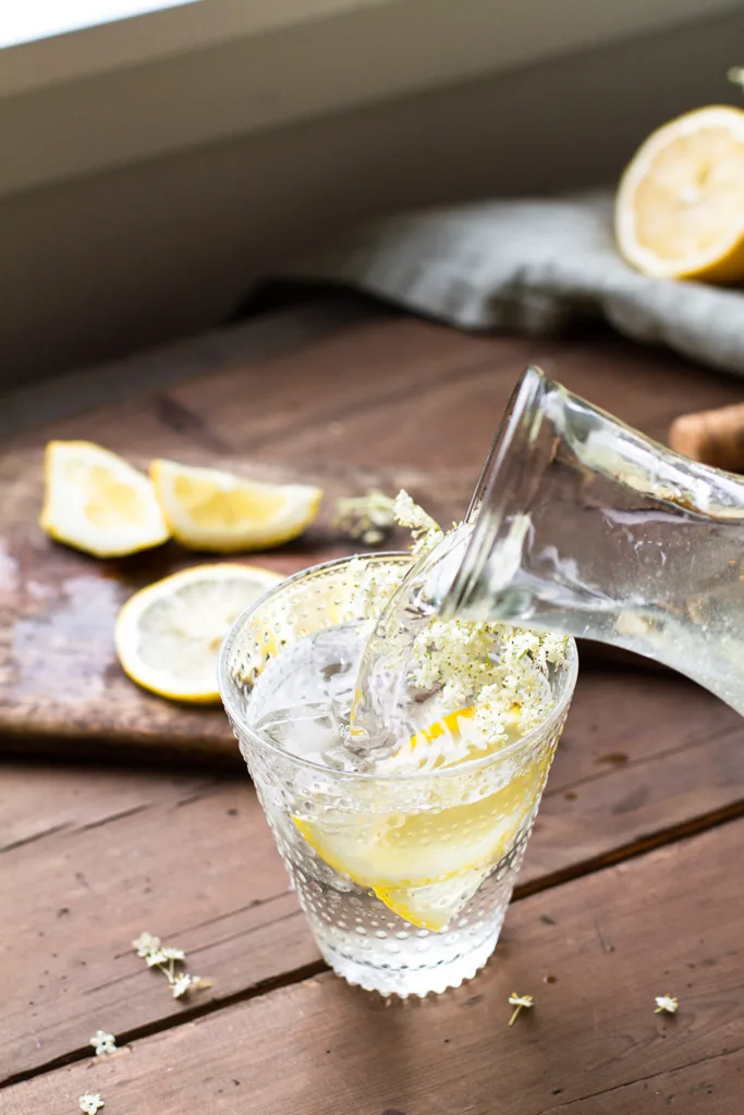 Pouring cordial into a glass with lemon wedge.