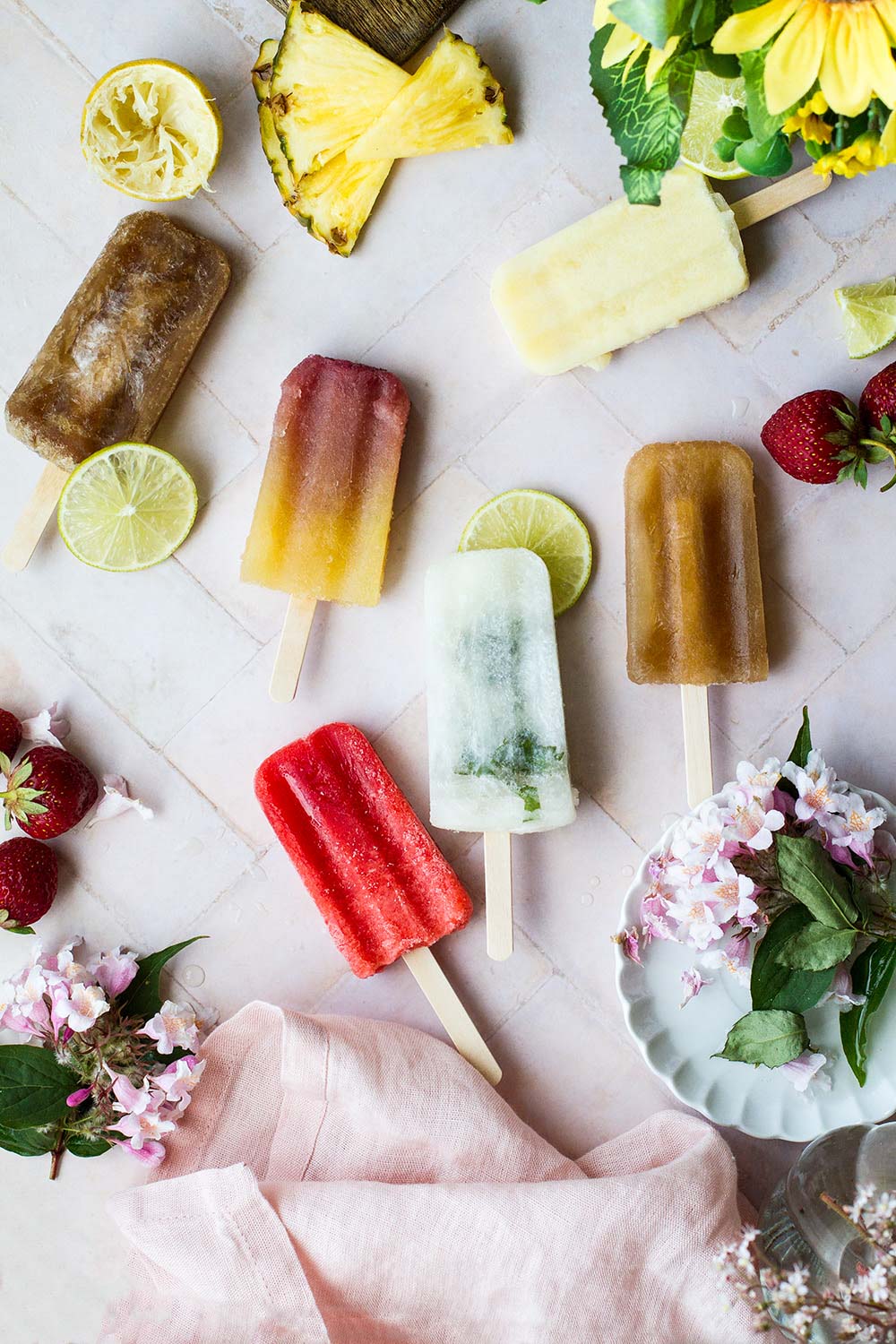6 different popsicles laying on a vintage tiled countertop.