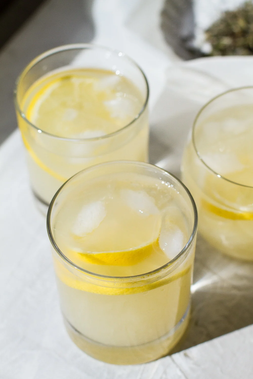 Three glasses with a yellow colored drink and lemon slices.