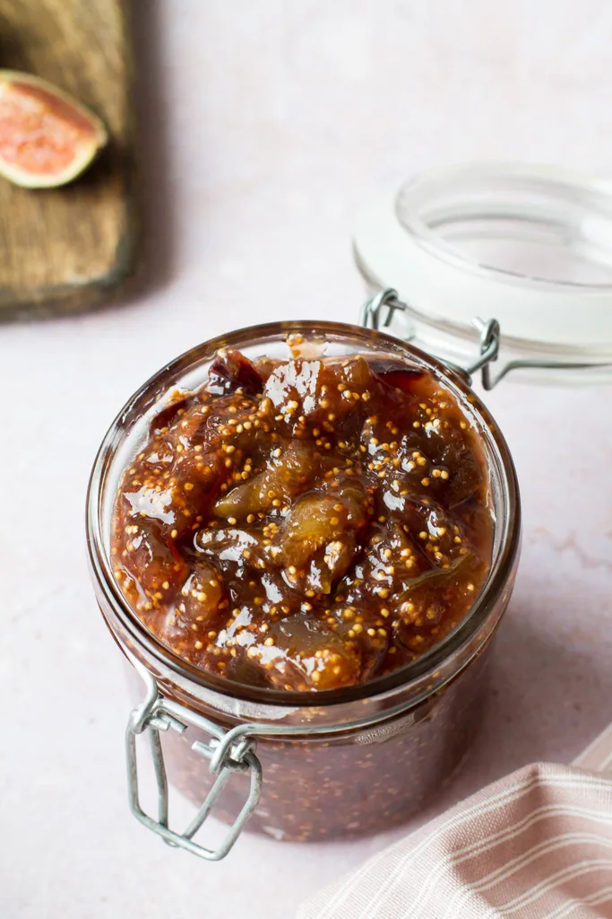 Fig jam in a glass jar, figs in the background.