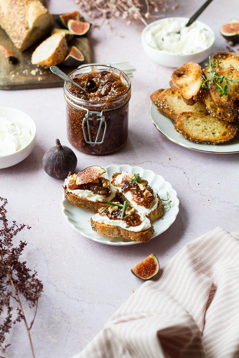 Three topped crostini and a jar of fig jam in the background.