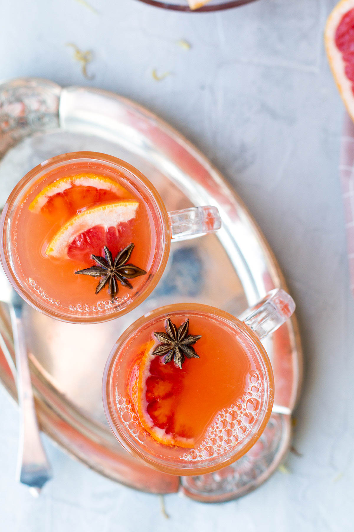 Two glasses with orange cider, garnished with grapefruit wedges and star anise. Seen from above.
