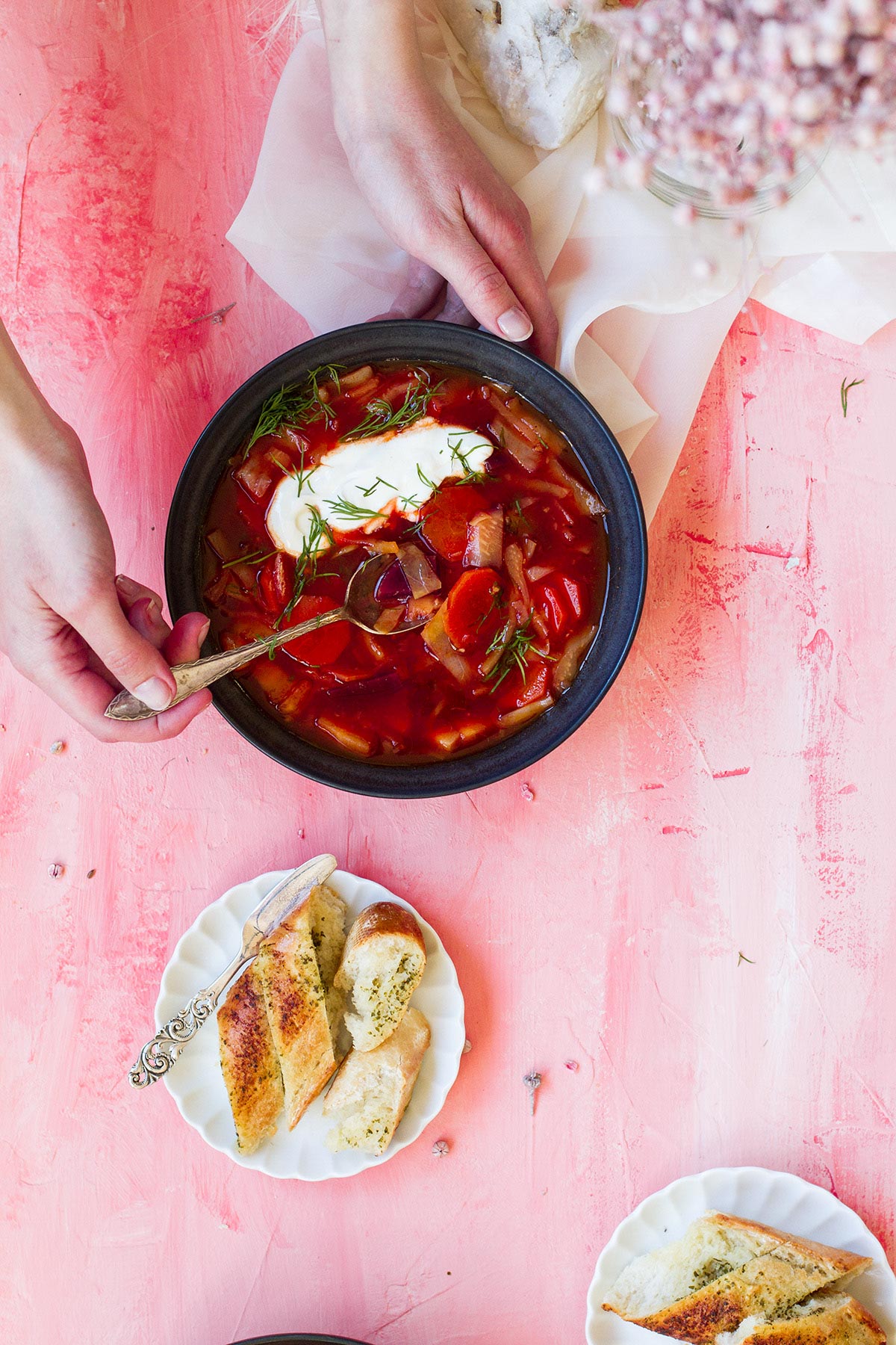 Hands holding a black bowl with bright red vegetable soup and sour cream.