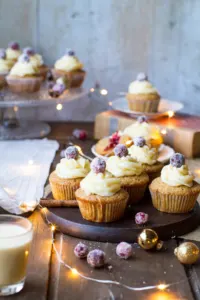 Gingerbread cupcakes on a wooden plate, topped with eggnog icing and sugar cranberries. Sparkling lights.