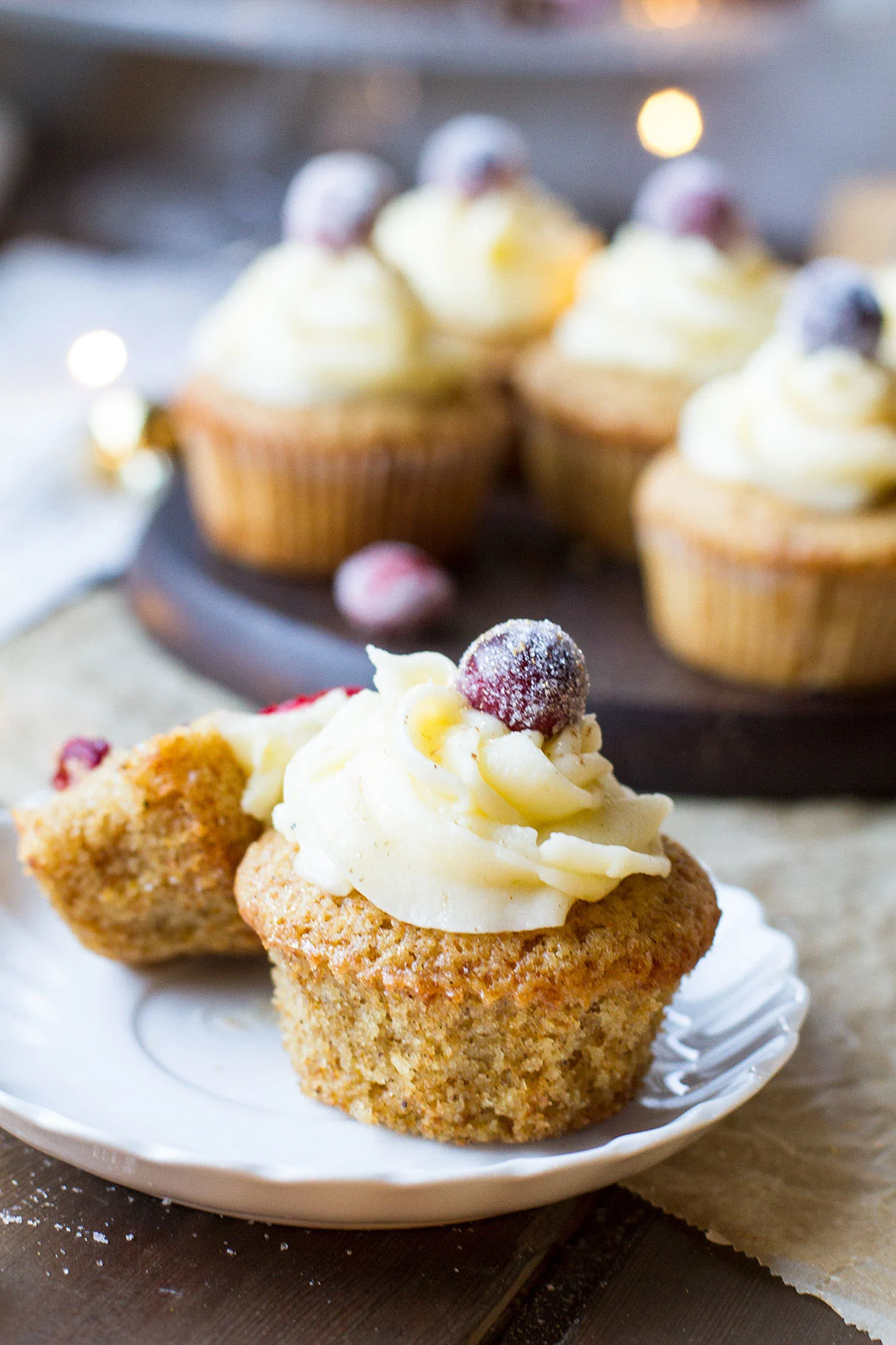 One cupcake with eggnog icing and sugar cranberry on top, out of its muffin liner.