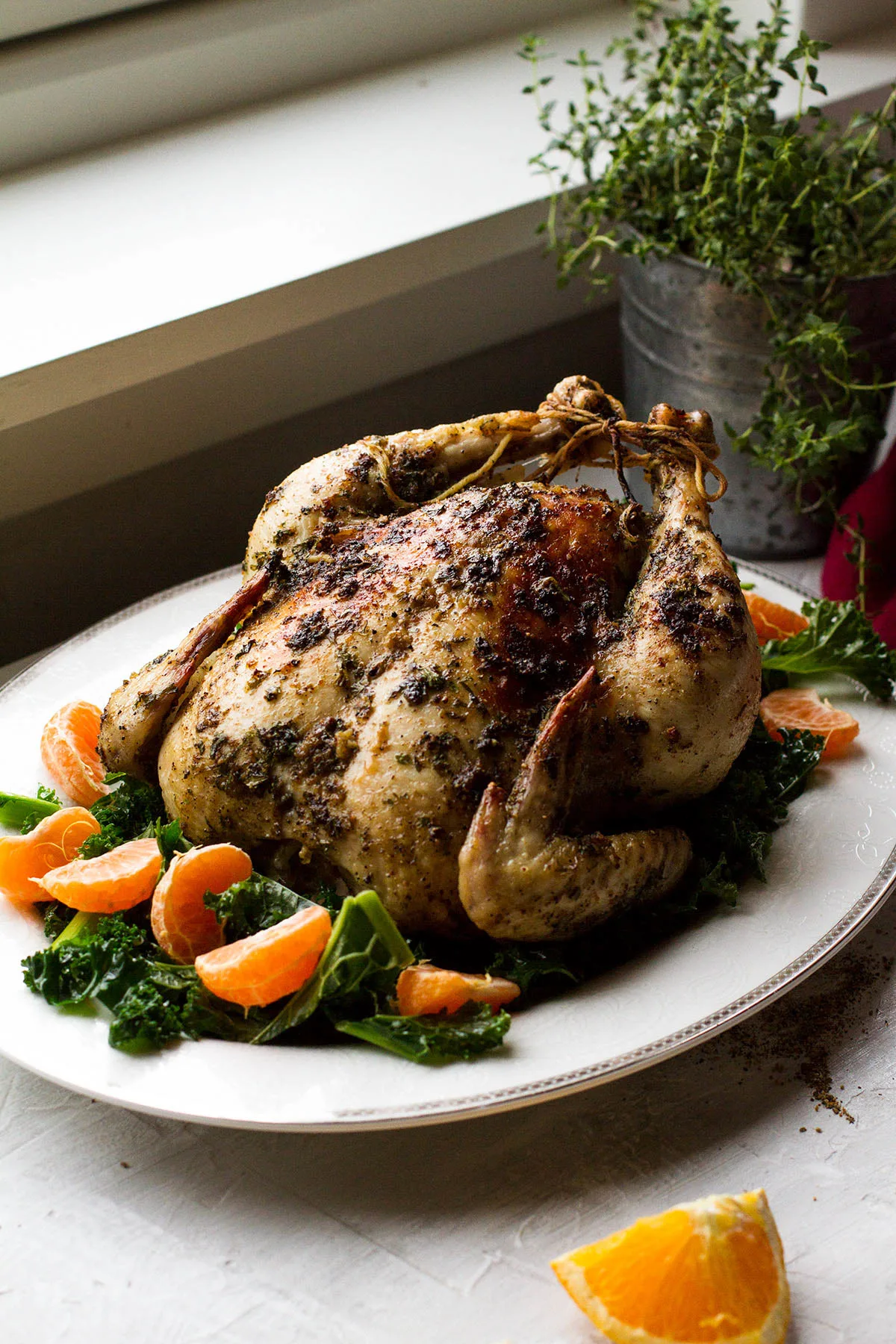 Whole roasted chicken on a bed of kale and clementines, backlighting.