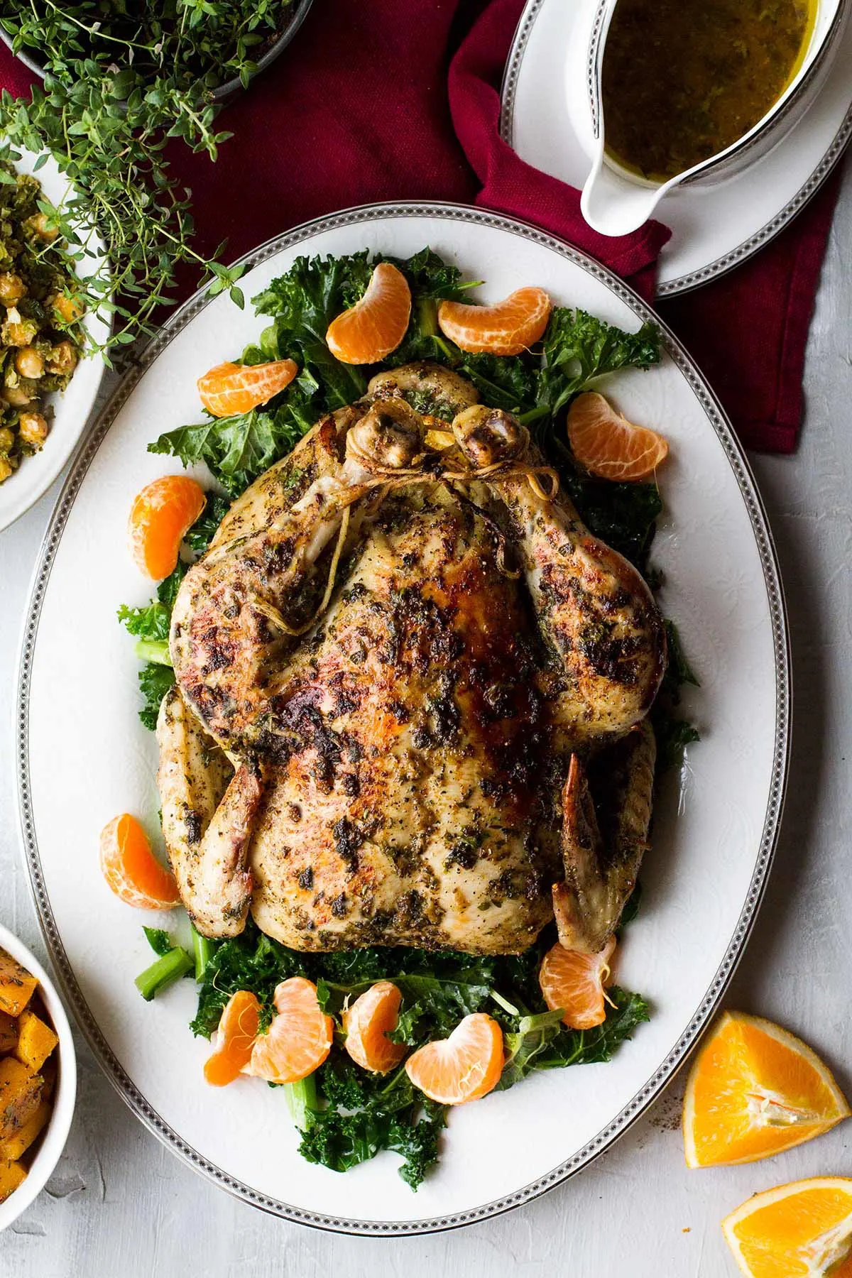 Whole roasted chicken on a bed of kale and clementines, flatlay.