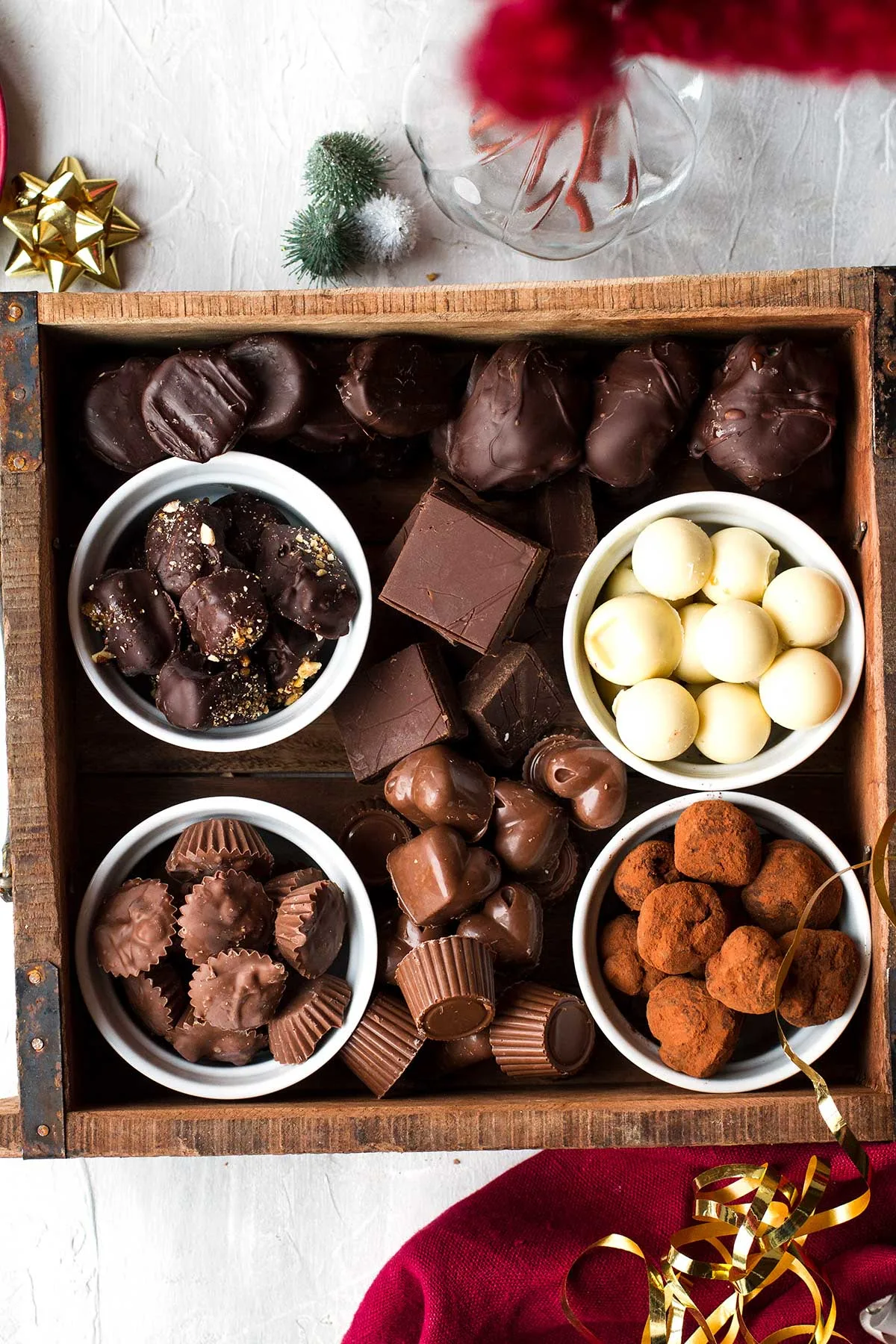 A wooden crate with 4 ramekins with chocolates and more around them.