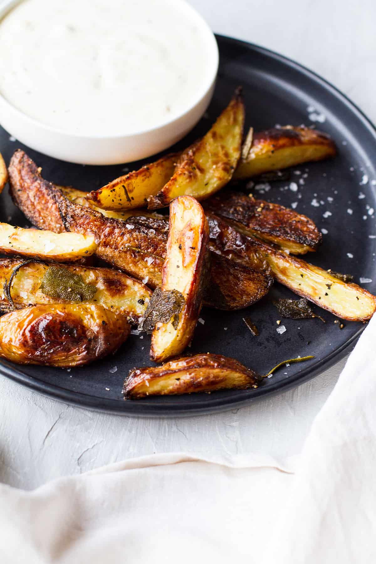 Close-up of crispy potato wedges with sage leaves.