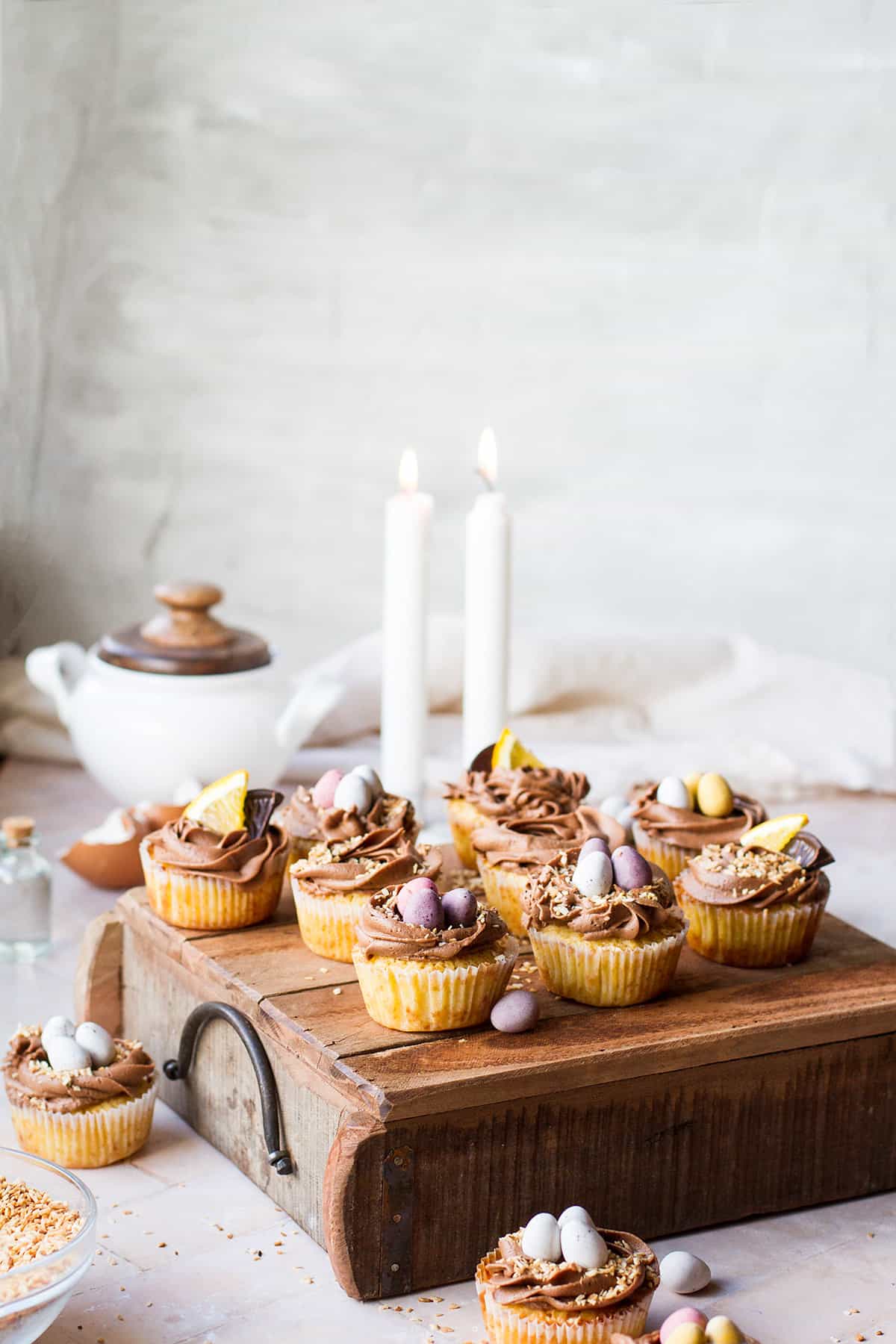Coconut cupcakes and chocolate frosting on a wooden tray.