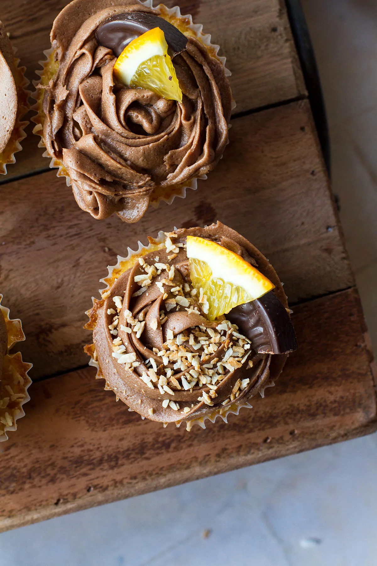 Flat-lay of a cupcake with chocolate buttercream, toasted coconut and an orange wedge.