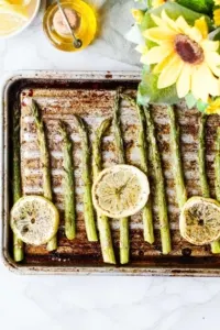Roasted asaparagus on an old baking sheet with three lemon slices.