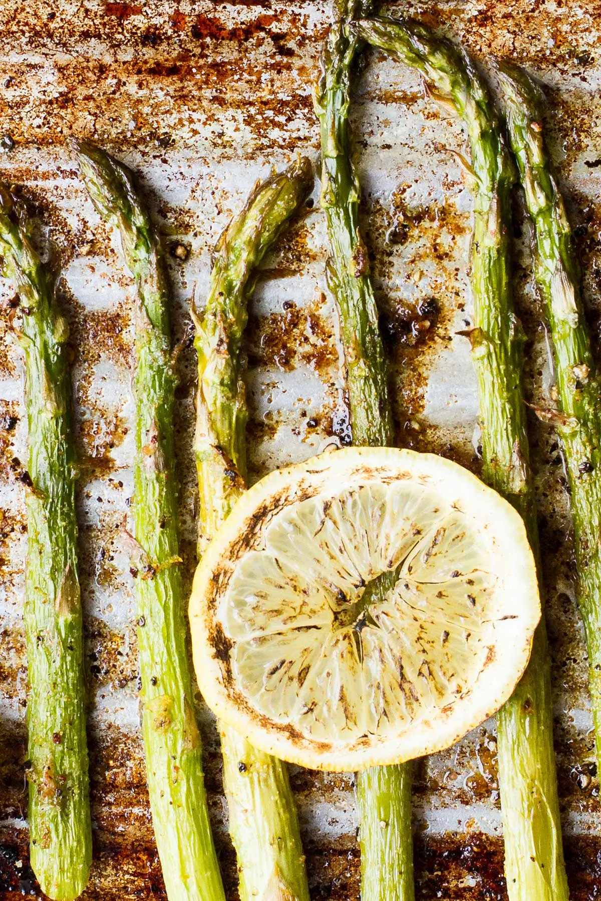 Close-up of roasted asparagus on a baking sheet with torched lemon slice.