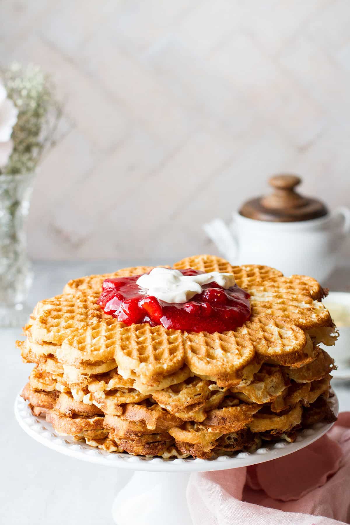 Tall stack of waffles on a cake stand.