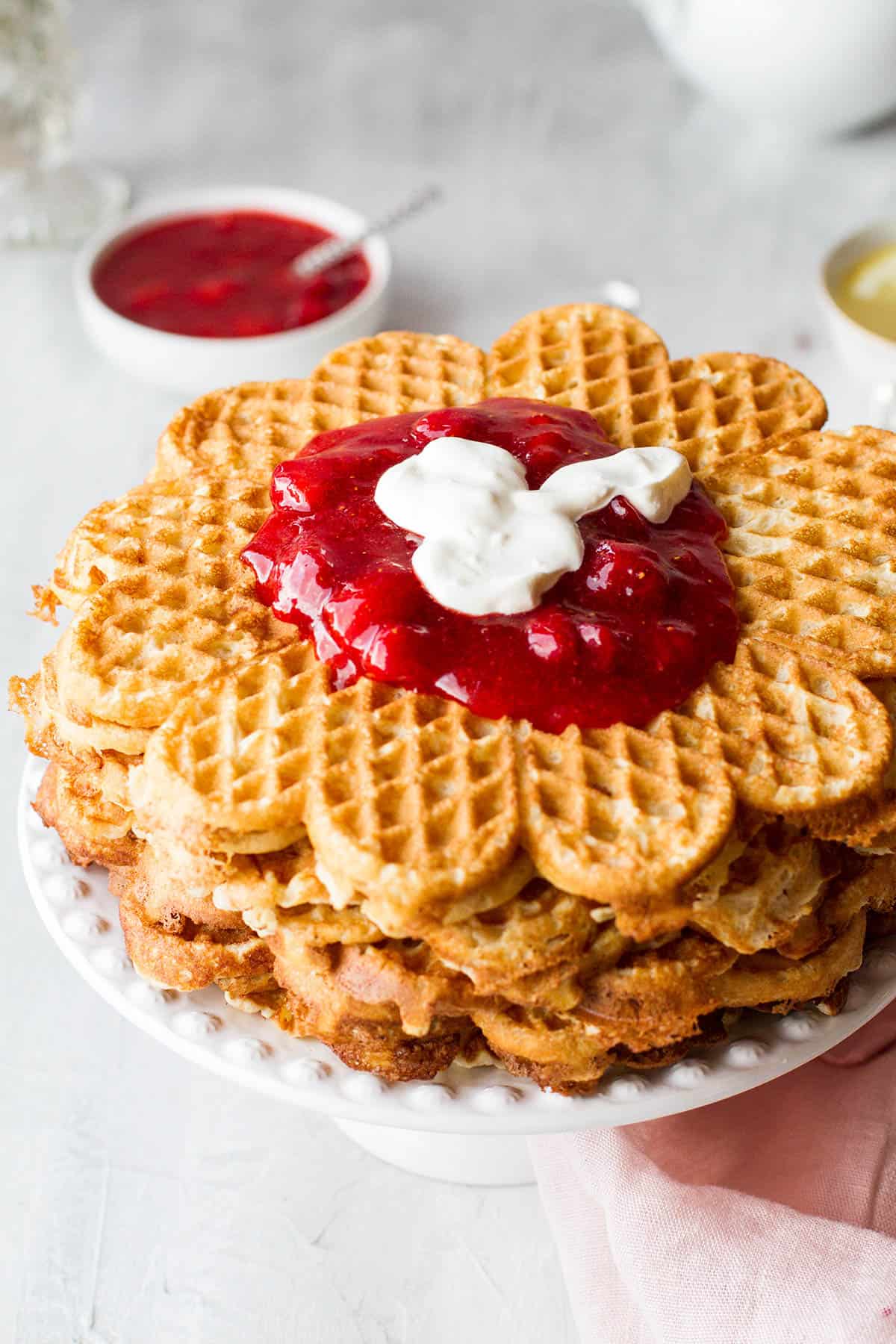 A stack of heart shaped waffles with strawberry jam and sour cream on the top.
