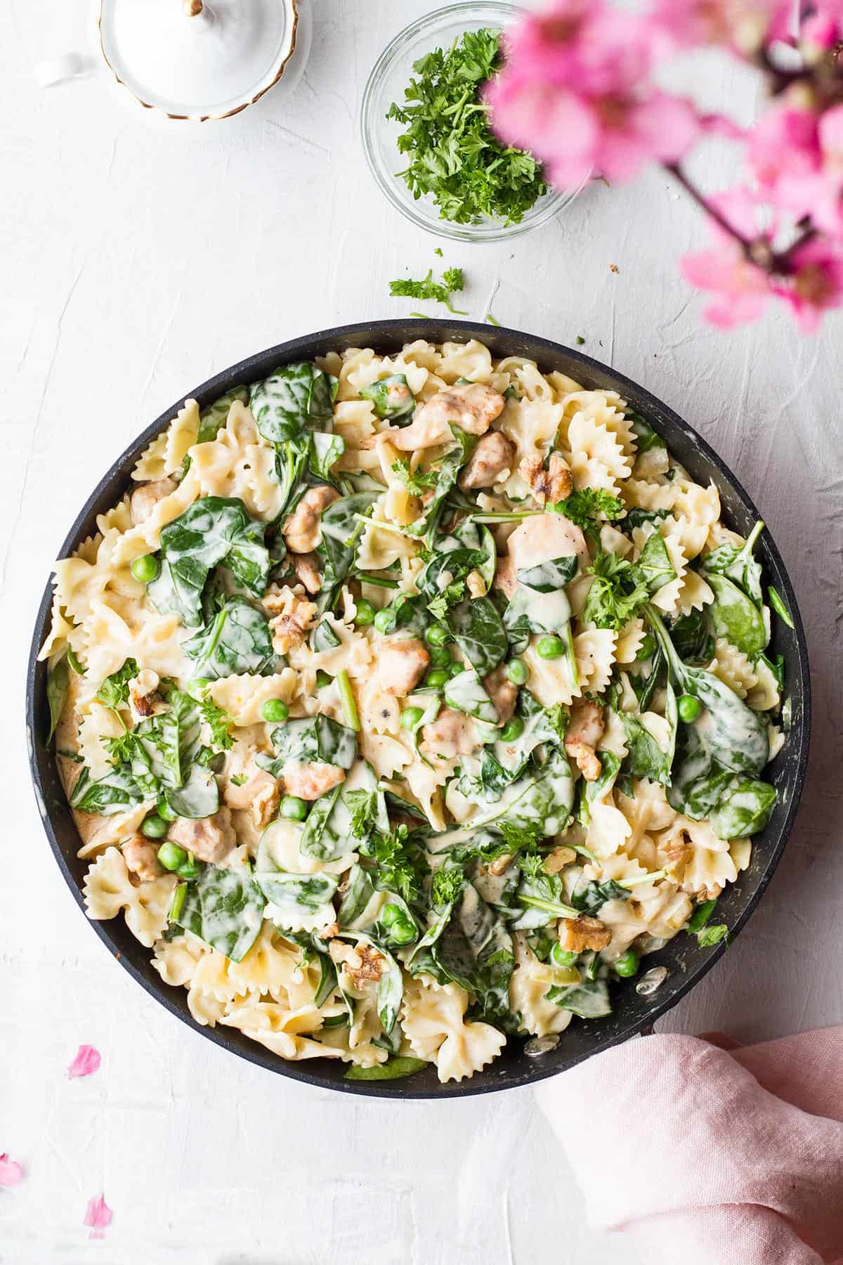 Skillet with pasta, peas, spinach and a cream sauce, seen from above.