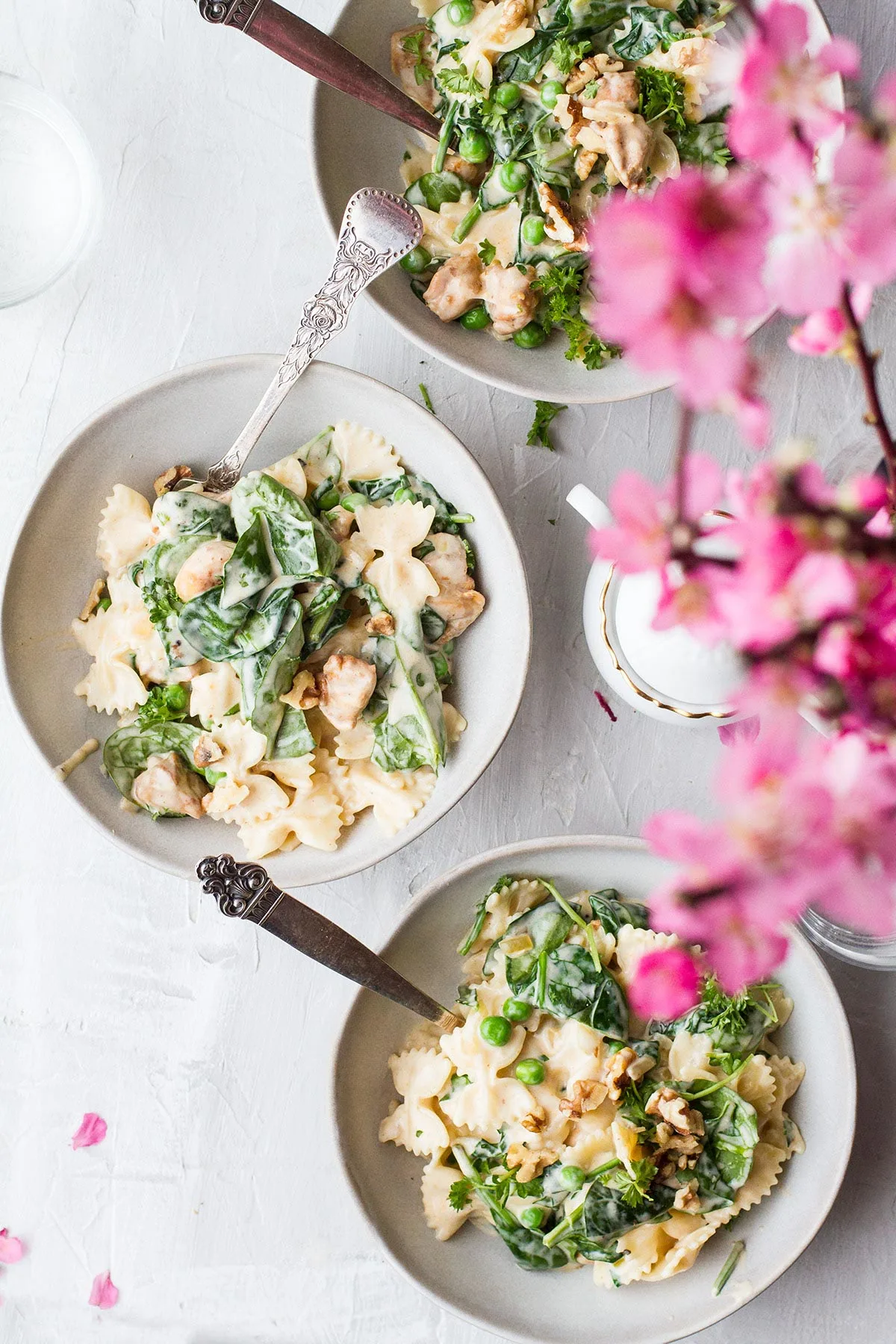 Three bowls with pasta and peas, pink flowers in the foreground.