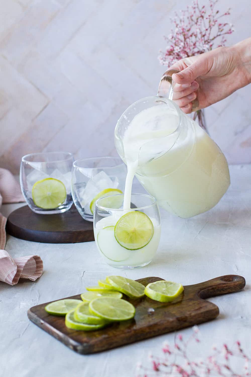 Pouring white lemonade into a round glass with lime wheels.
