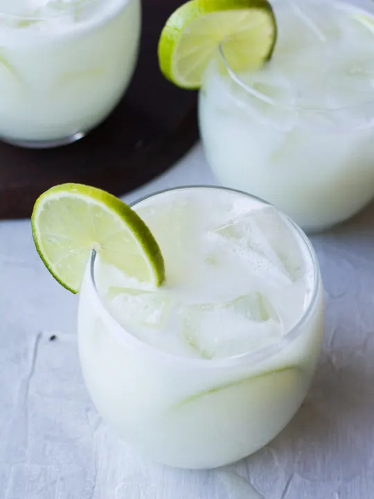 Close-up of a glass filled with ice and Brazilian lemonade, garnished with lime.