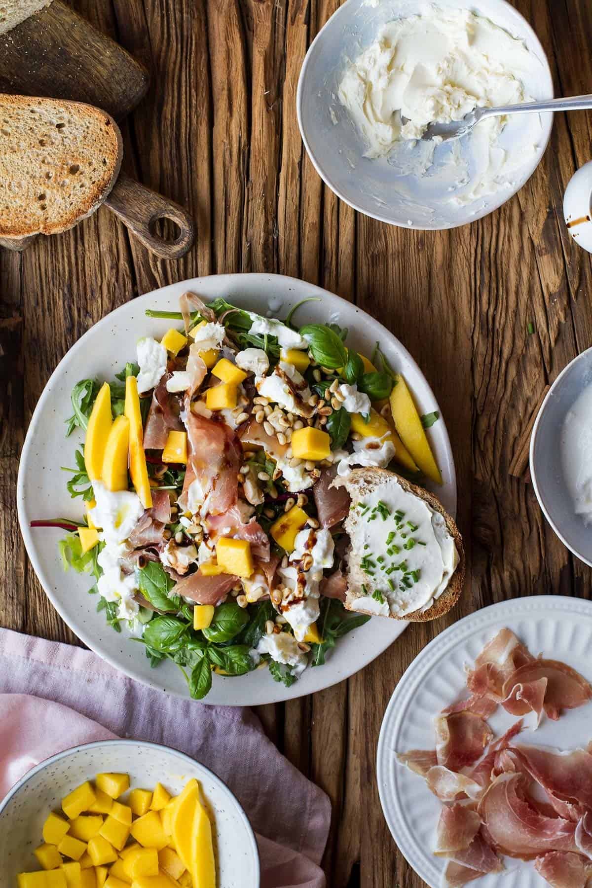 A large plate of burrata and prosciutto salad on an old wooden table.