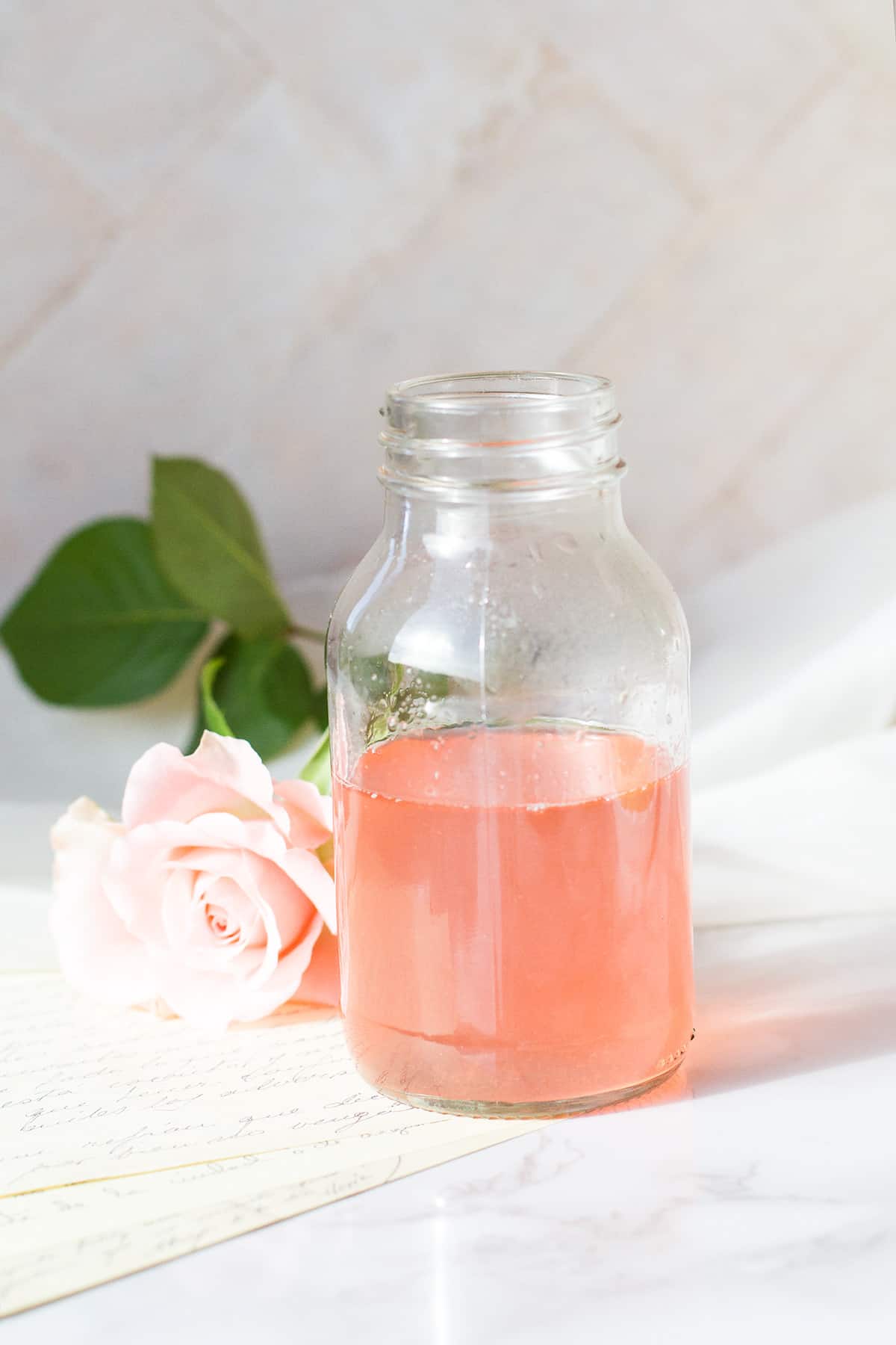 Rhubarb syrup in a glass bottle, pink rose in the background.