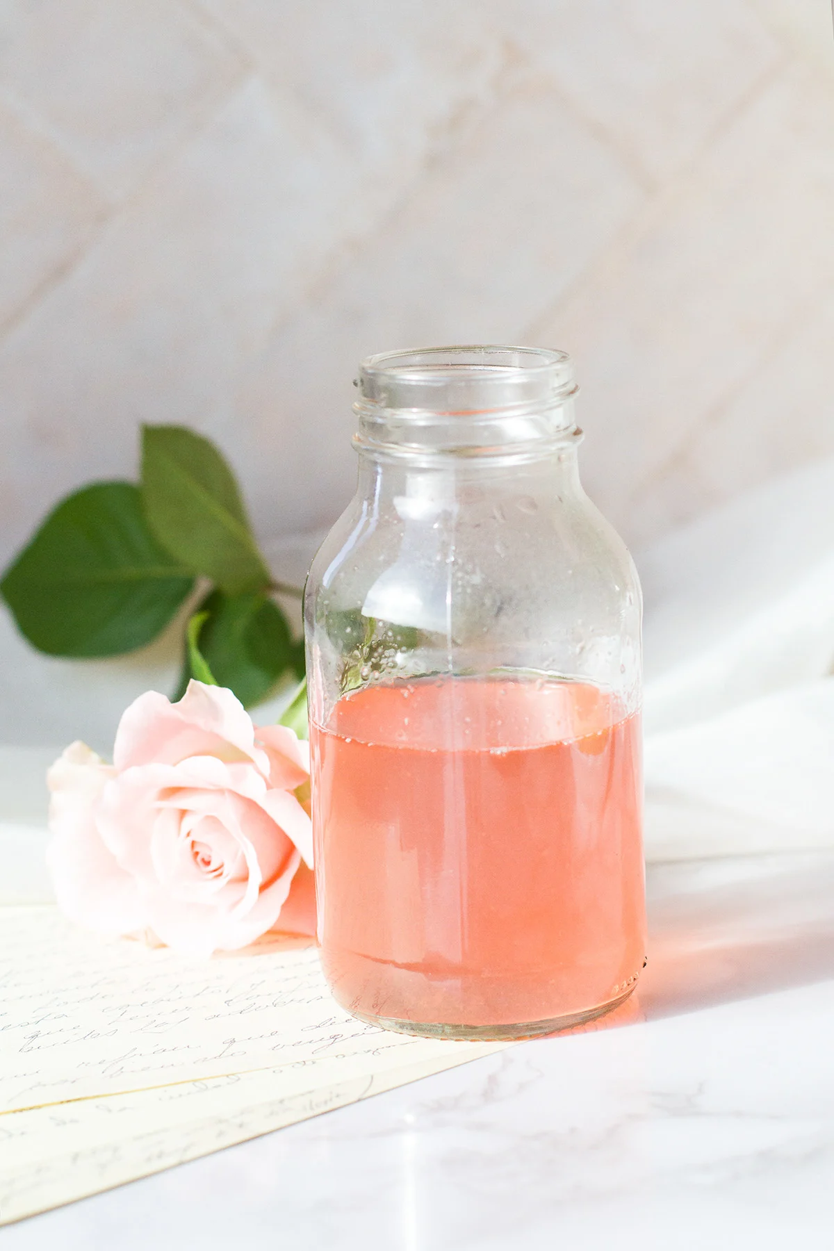 Rhubarb syrup in a glass bottle, pink rose in the background.