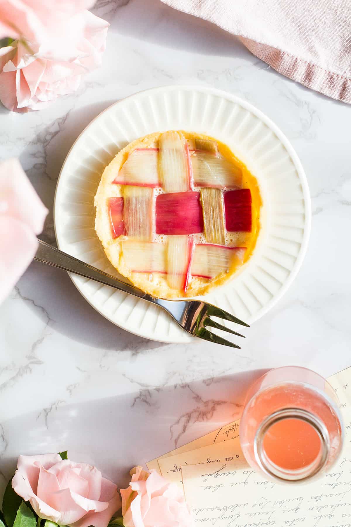 Tart with strips of rhubarb like a lattice pattern, bottle with rhubarb syrup on the side.