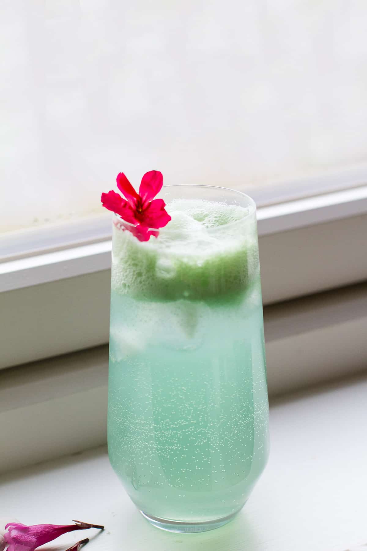 A tall glass with cucumber gin and tonic and a fresh, pink flower.
