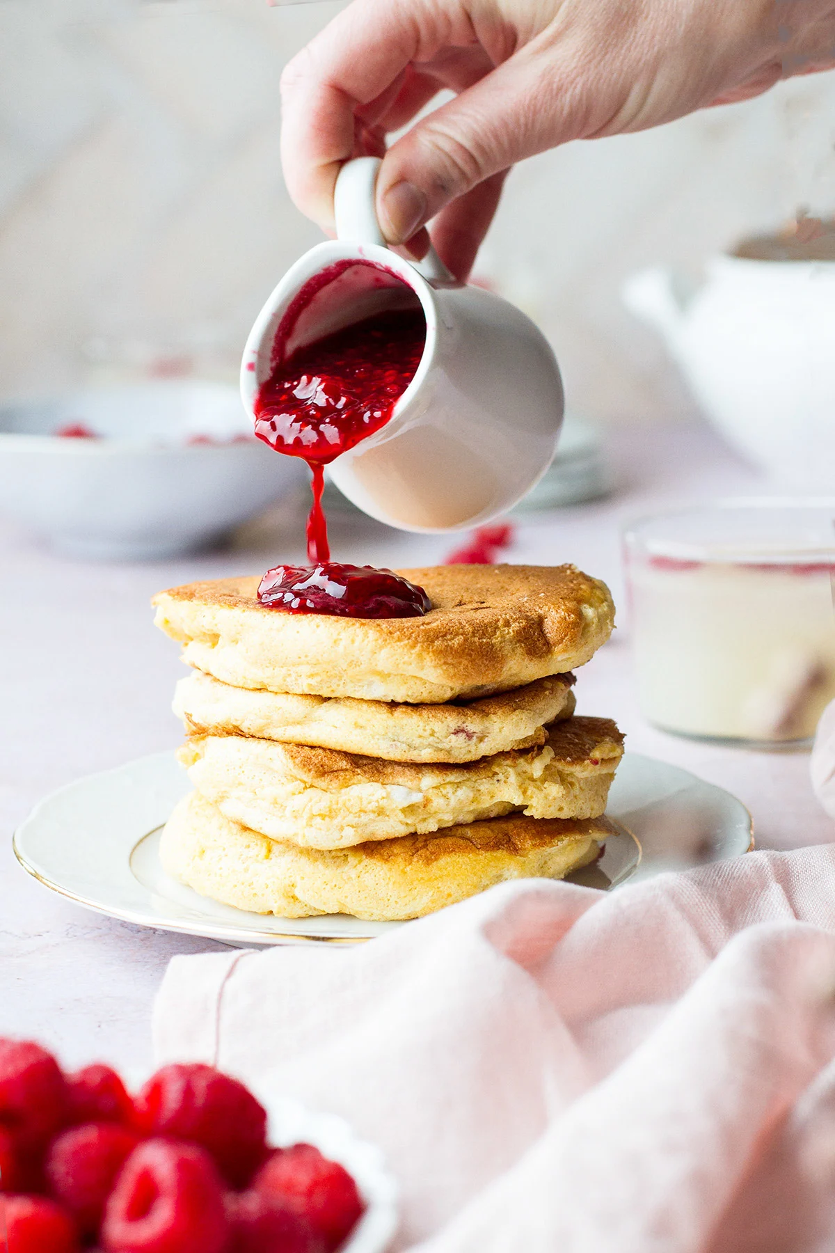 Pouring raspberry sauce over fluffy pancakes.