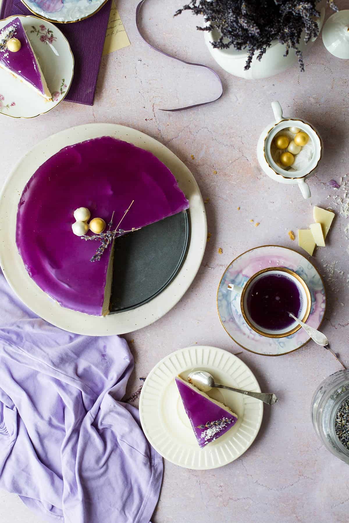 Whole cheesecake with purple jelly lid, three slices taken out of it and put on vintage plates.