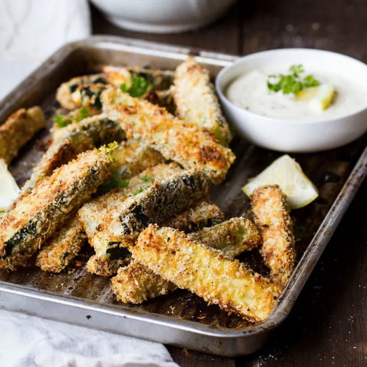 An old baking tray with zucchini sticks and dipping sauce.