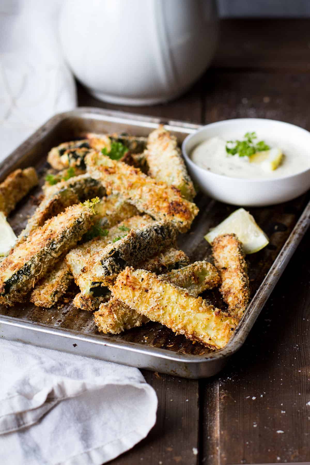An old baking tray with zucchini sticks and dipping sauce.