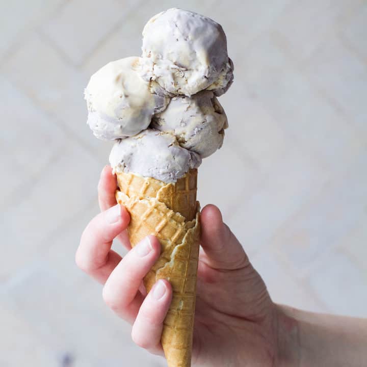 Hand holding a waffle cone with four scoops of Earl Grey ice cream.