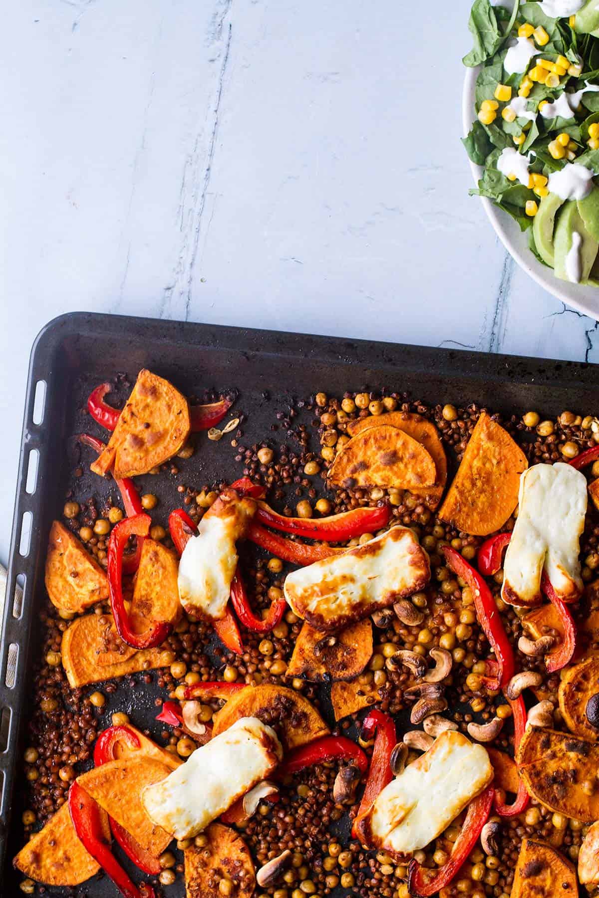 Sheet pan with sweet potato and halloumi seen from above.