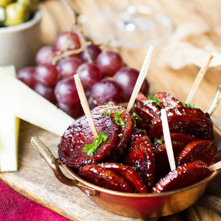 A small copper dish with red wine chorizo and toothpicks.