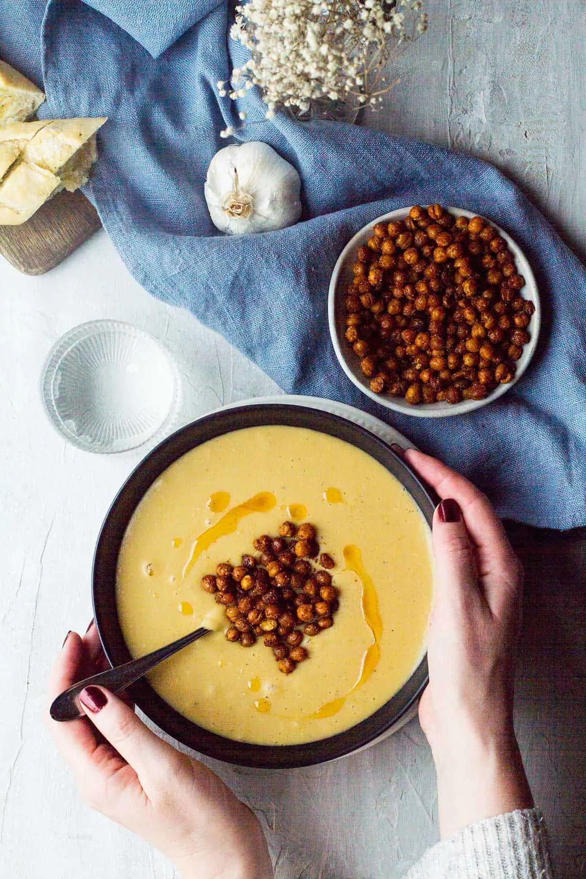 Hands holding a bowl of roasted garlic chickpea soup.