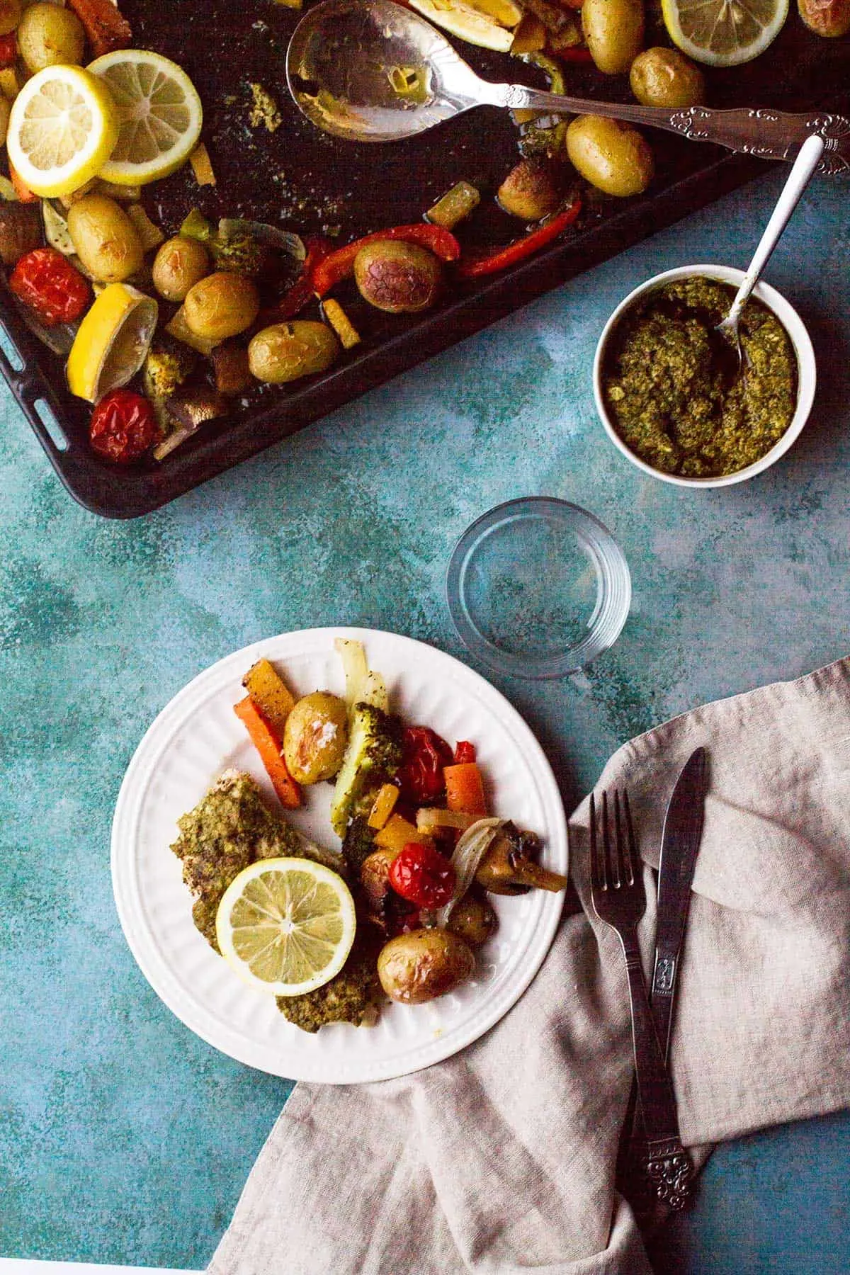 White plate with pesto chicken and roasted vegetables, seen from above.
