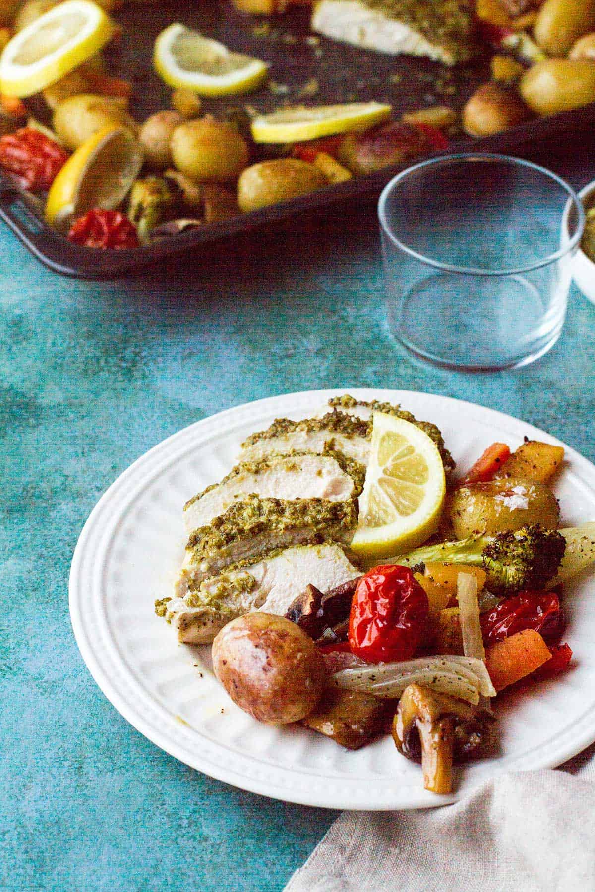 A white plate with sliced pesto chicken and baked vegetables.