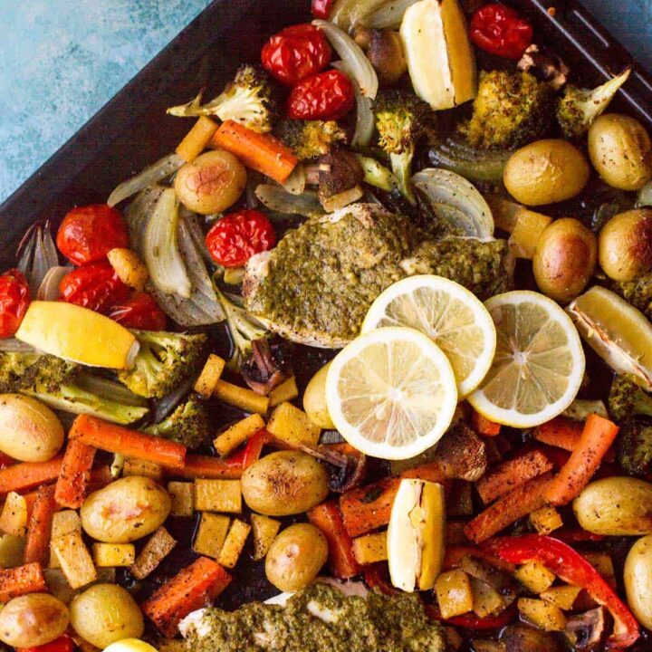 Close-up of the baking sheet with chicken and vegetables and sliced lemon.