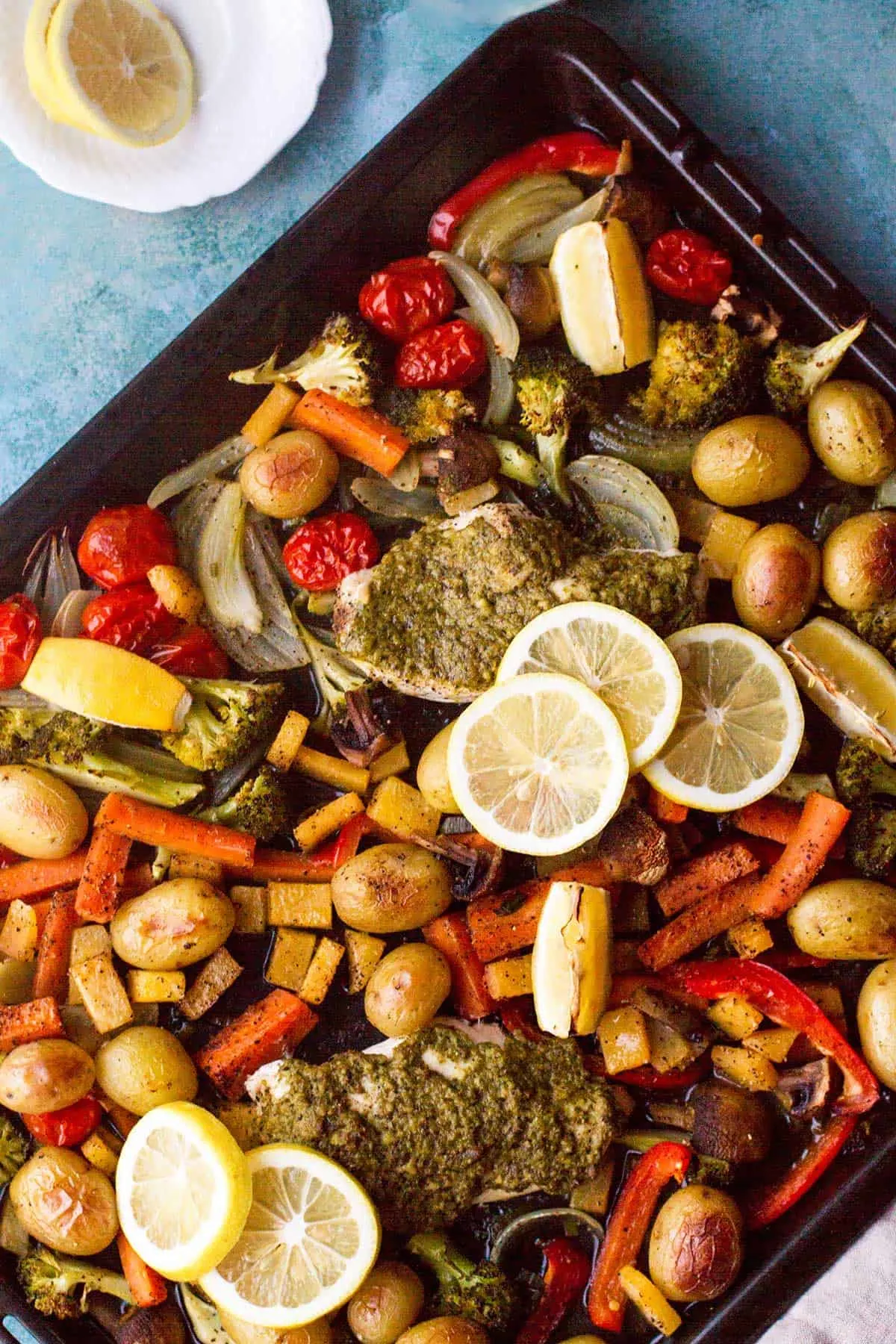 Close-up of the baking sheet with chicken and vegetables and sliced lemon.