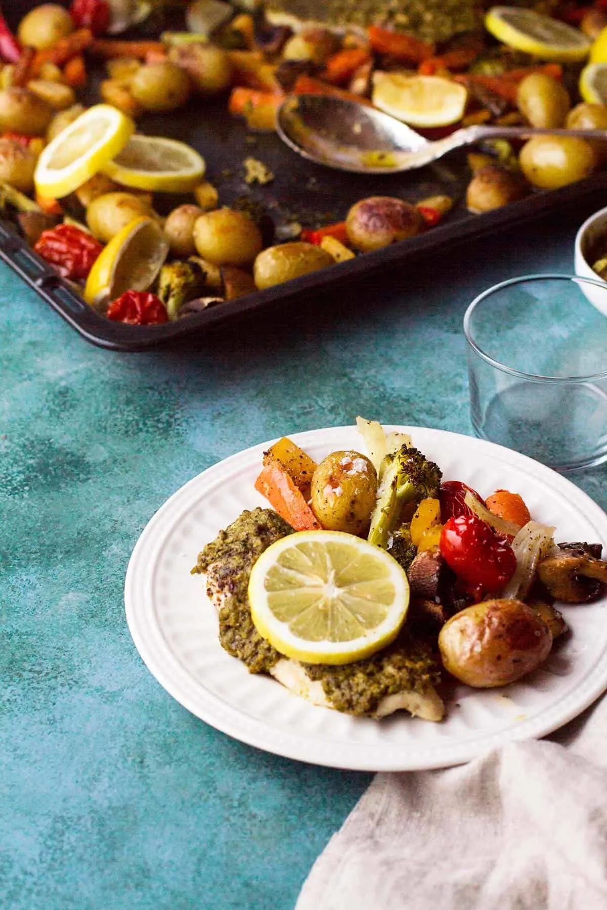A white plate with chicken and pesto and roasted vegetables.