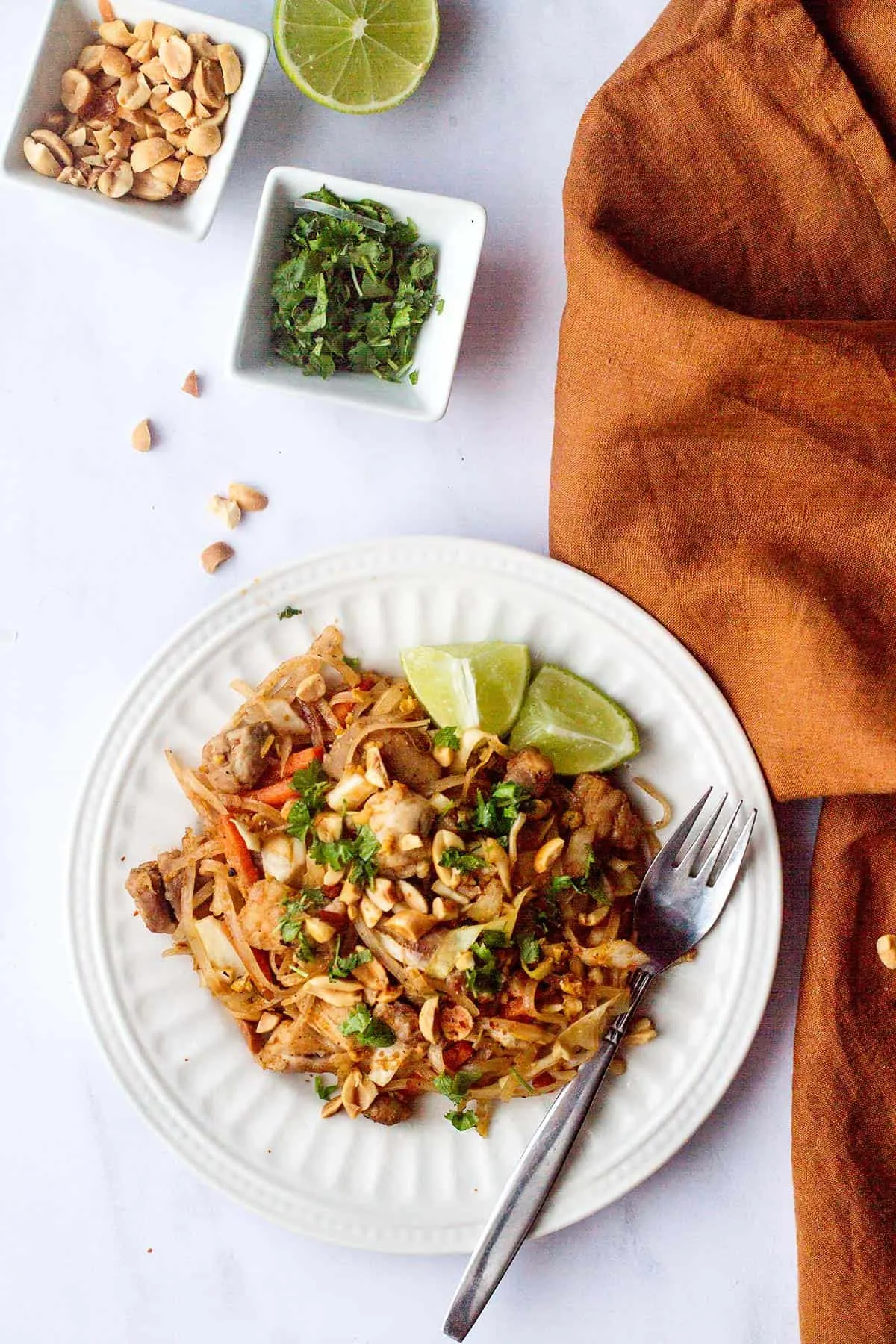 Serving suggestion of chicken and cabbage pad thai with lime and peanuts.