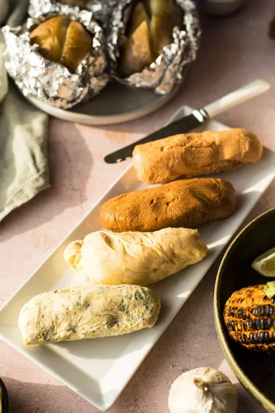 Four logs of compound butters on a white plate.