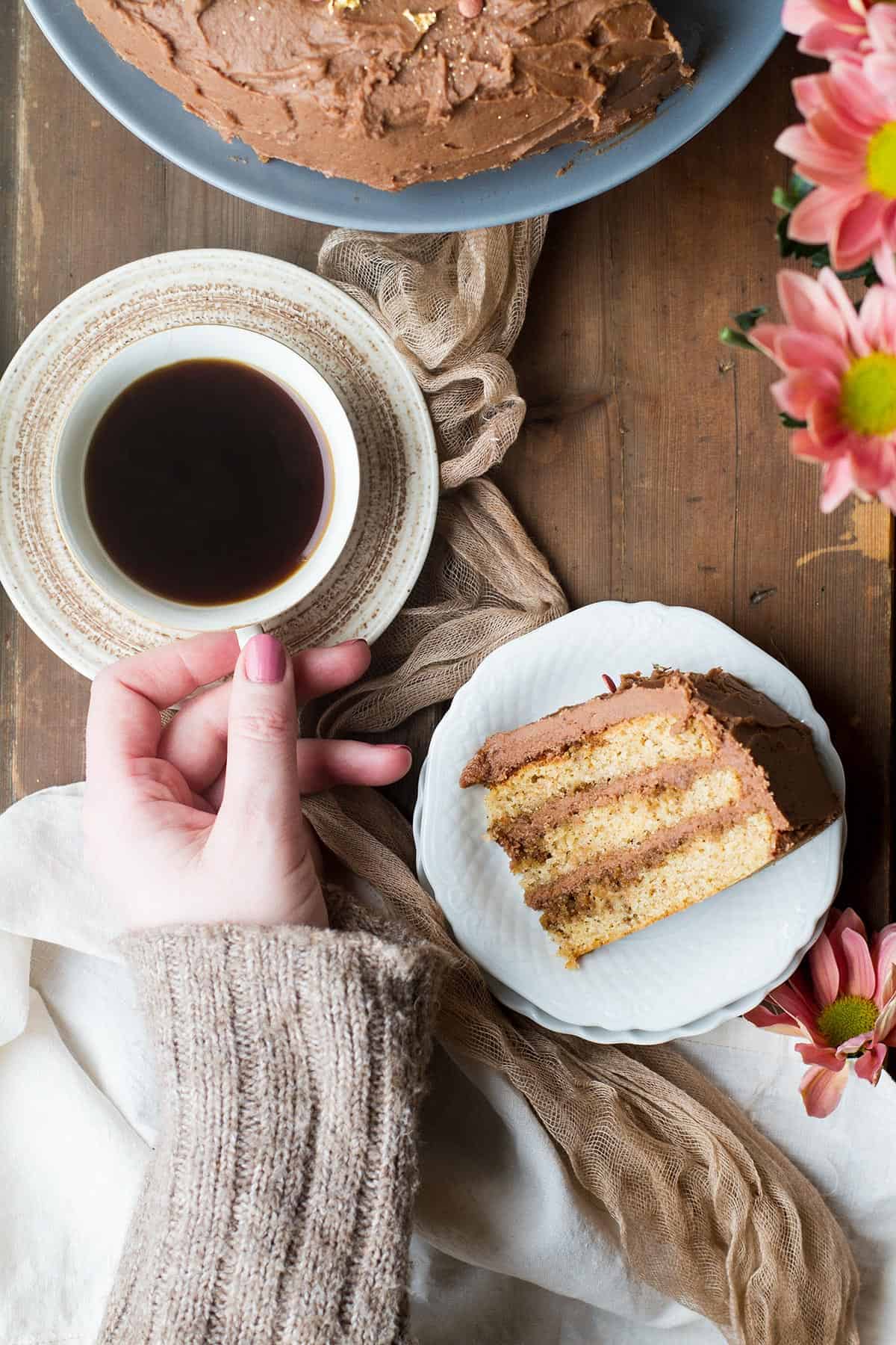 Hand holding a cup of coffee, a slice of spice cake next to it.