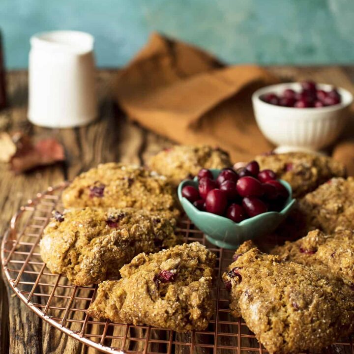 Pumpkin scones on a wire rack with cranberries in a small bowl.