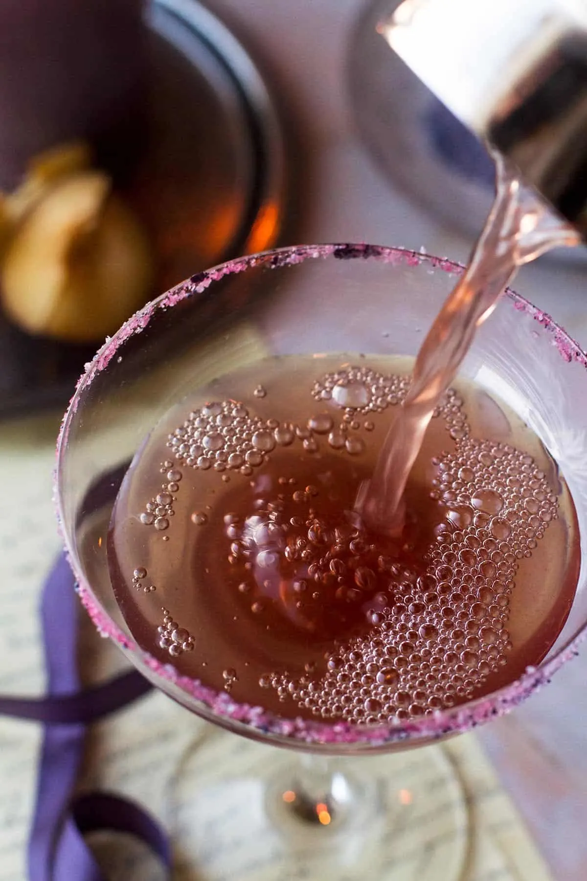 Pouring plum Halloween margarita in a cocktail glass.