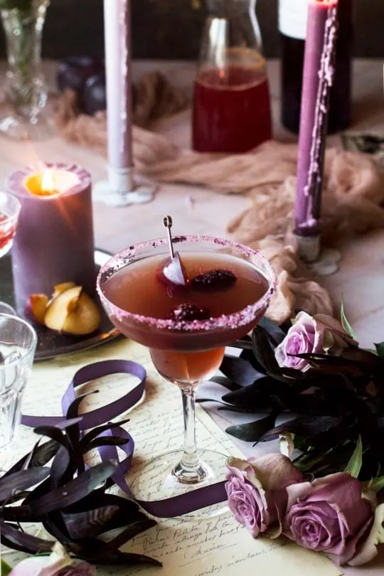 Plum Halloween margarita in a margarita glass. Purple roses and candles in the fore- and background.
