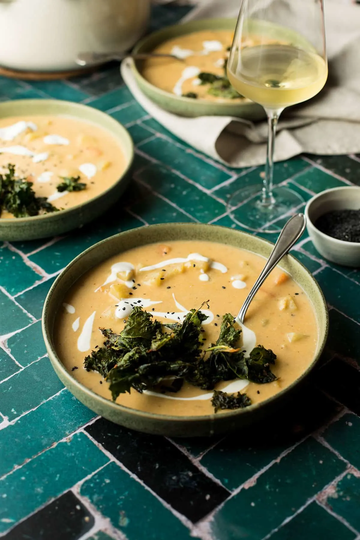 A shallow bowl of potato and carrot soup with kale chips.