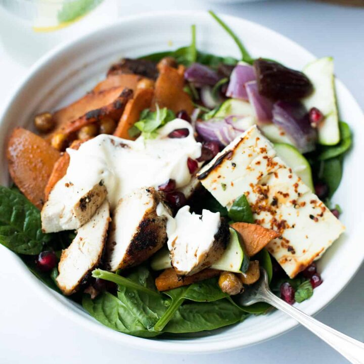 White bowl with fresh salad, baked feta cheese and roasted chicken.